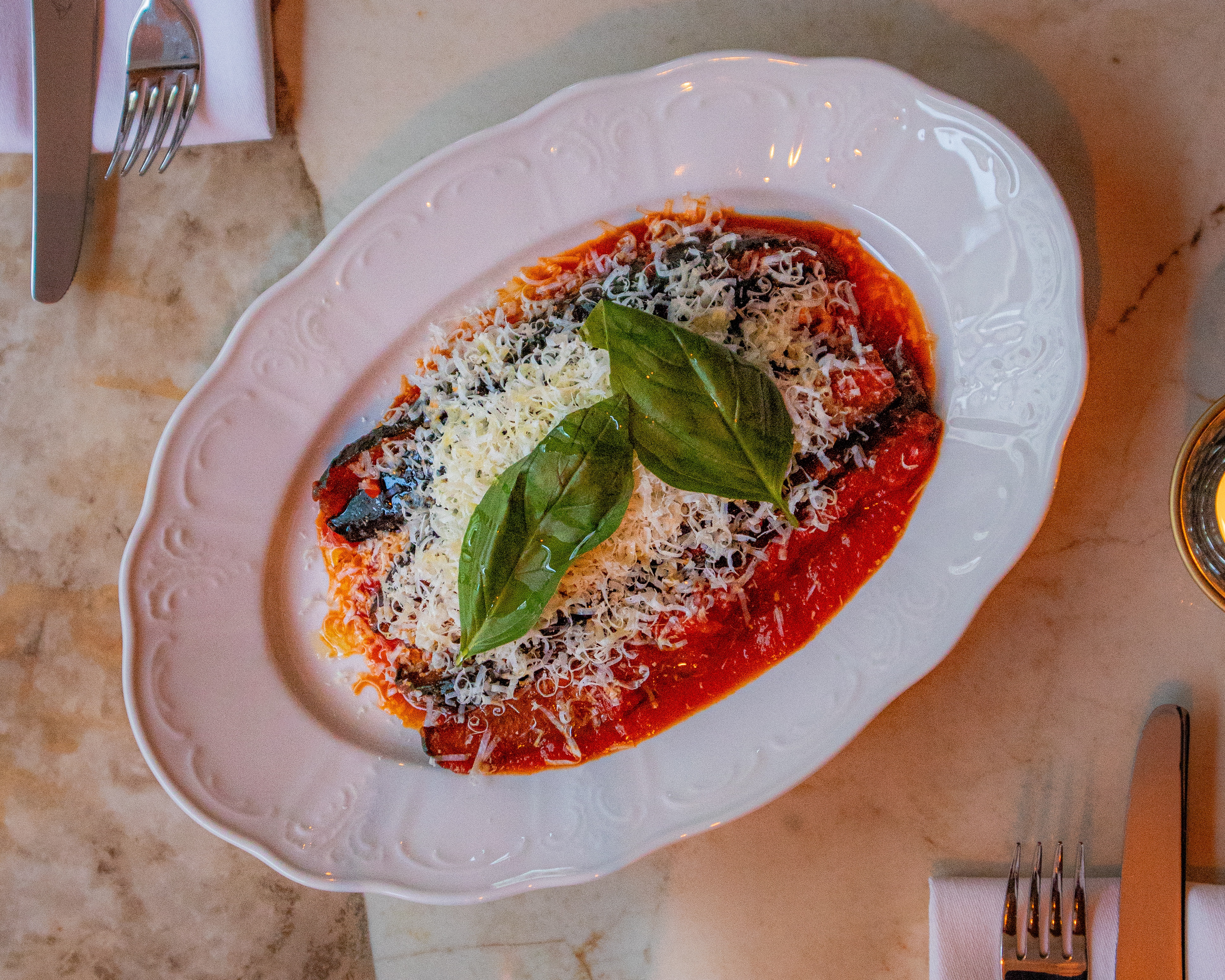 Überbackene Pasta in roter Tomatensauce, serviert auf einer weißen Platte und mit geriebenem Käse sowie frischem Basilikum garniert.