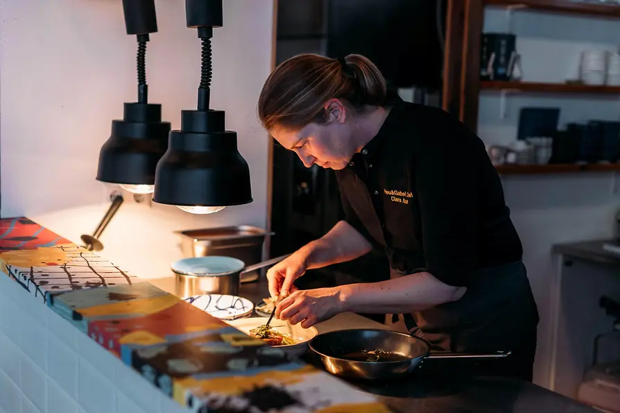 A chef carefully plates a dish in a restaurant kitchen under warm hanging lights.