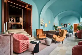 A vibrant lounge with turquoise vaulted ceilings, colorful mid-century–inspired seating, soft lighting, and framed artwork, creating a lively yet elegant atmosphere.