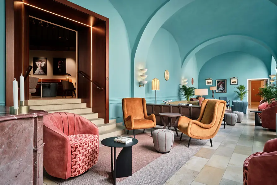 A vibrant lounge with turquoise vaulted ceilings, colorful mid-century–inspired seating, soft lighting, and framed artwork, creating a lively yet elegant atmosphere.