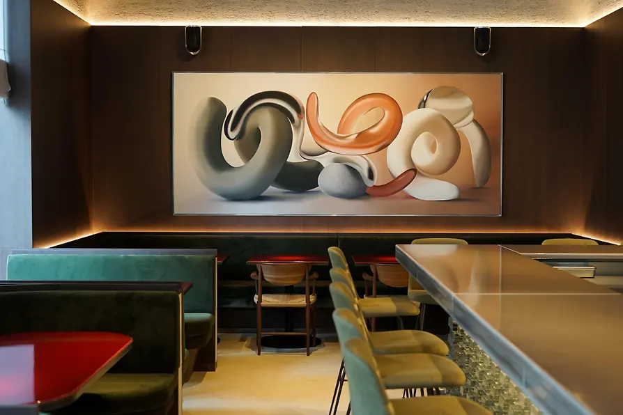 A stylish restaurant interior with green upholstered seating, a long counter, and a large abstract artwork featuring intertwined sculptural forms.
