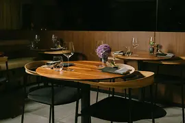 Ein warm beleuchtetes Restaurant mit Holztischen, elegantem Glasgeschirr, schwarzen Stühlen und violetten Blumenarrangements.