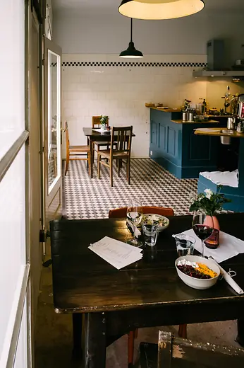Small restaurant with wooden tables, patterned tile floor and open kitchen.