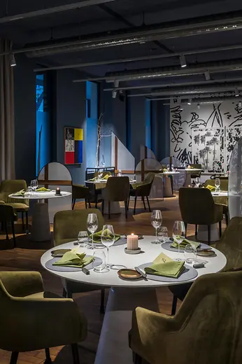 Modern restaurant with round tables, green chairs and ambient lighting.