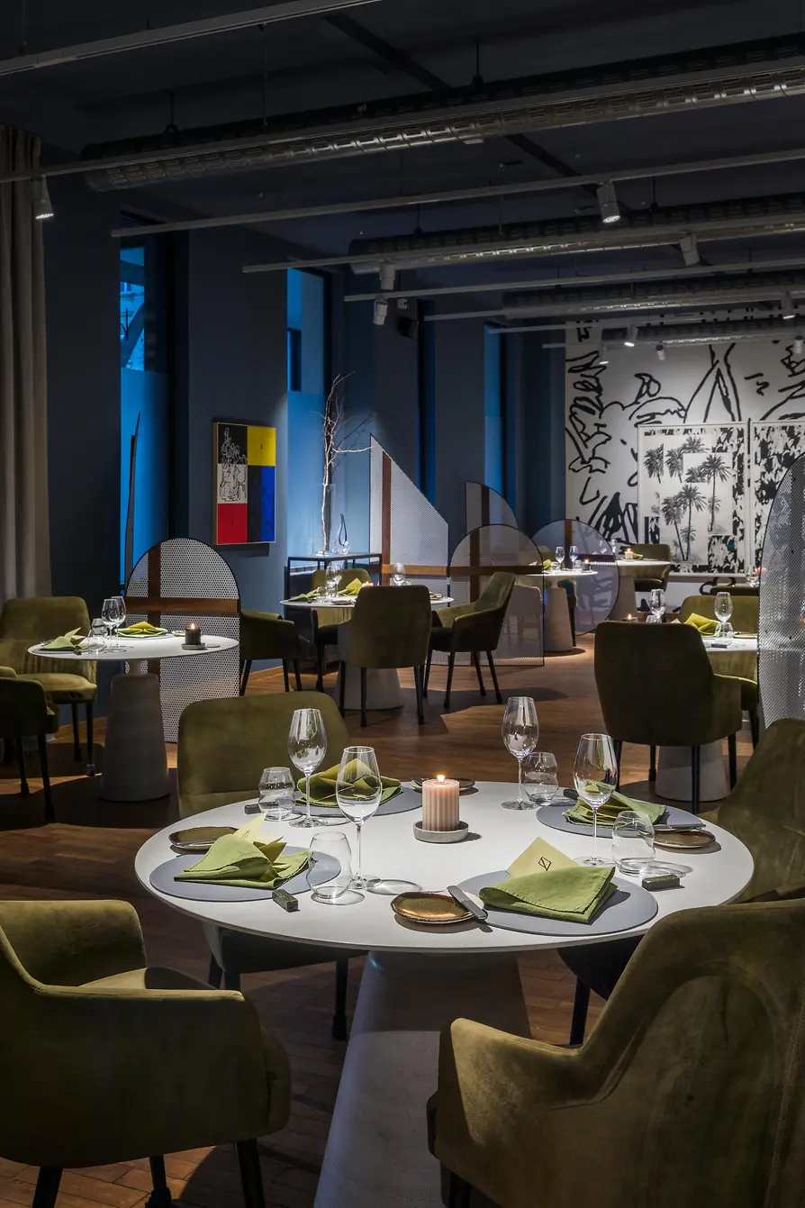 Modern restaurant with round tables, green chairs and ambient lighting.