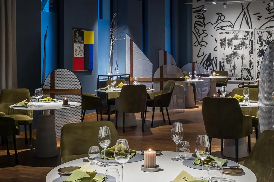 Modernes Restaurant mit runden Tischen, grünen Sesseln und stimmungsvoller Beleuchtung.