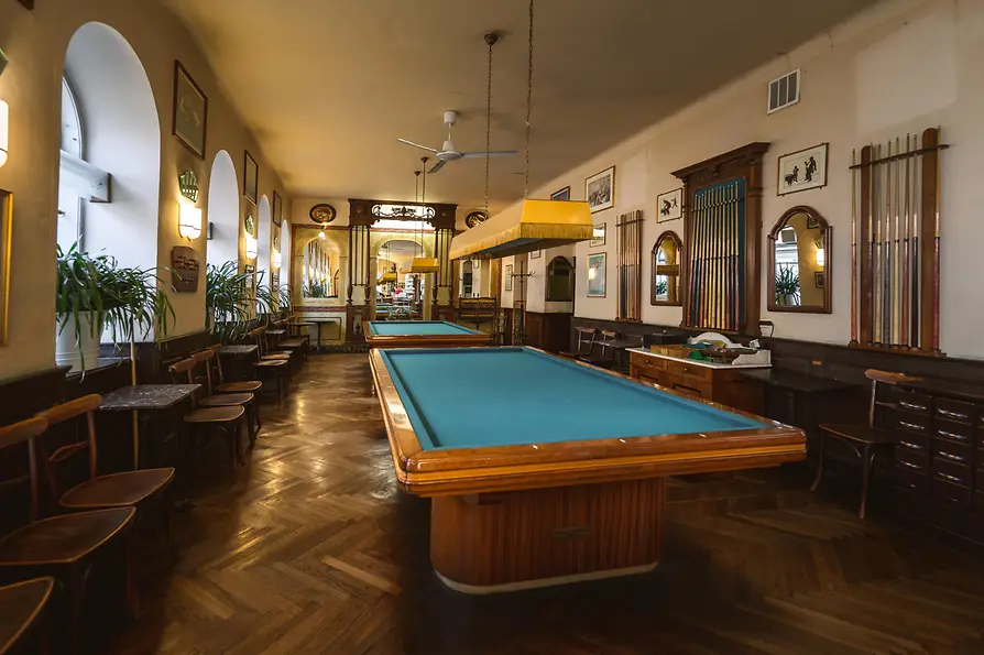 Historischer Billardsaal mit zwei Tischen, Holzvertäfelung und Queue-Wänden.