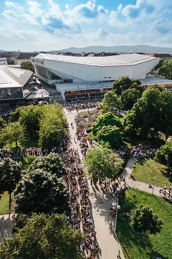 Aerial view of Vienna’s Stadthalle with a large crowd gathered outside and green park areas surrounding it.