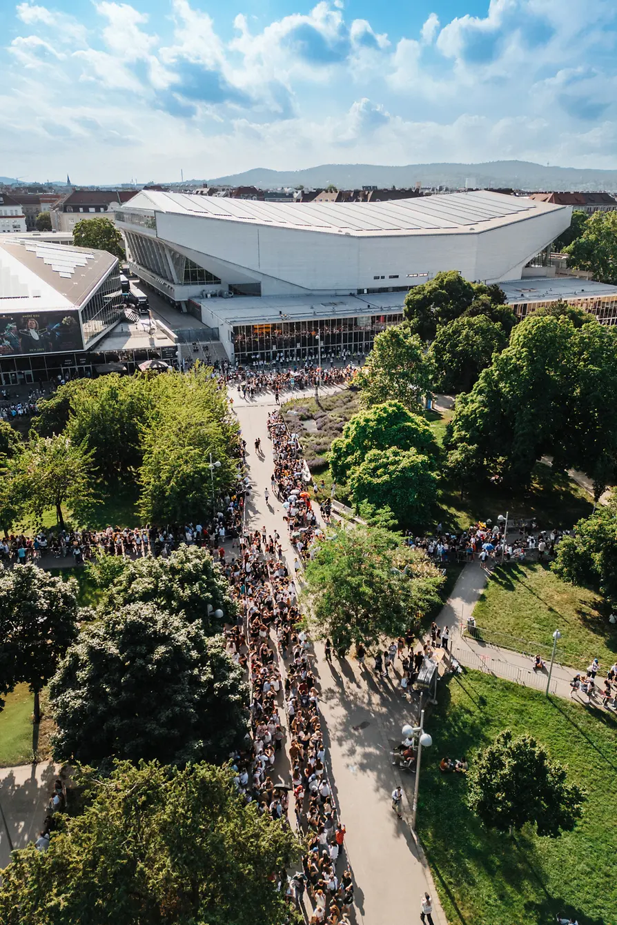 Aerial view of Vienna’s Stadthalle with a large crowd gathered outside and green park areas surrounding it.