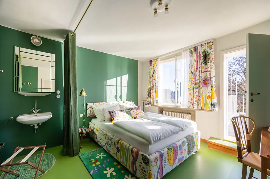 Guest room with colorful textiles, green floor, and view of the balcony.