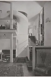 Historic view of the entrance hall with curved staircase and gallery.