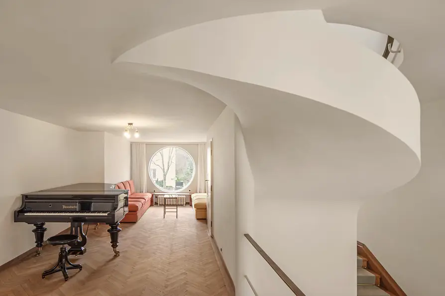 Music room with grand piano, circular window opening, and seating.