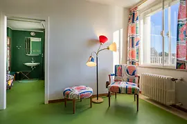 Seating area in the guest room with patterned armchair and floor lamp.