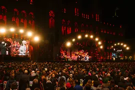 Large open-air concert in front of a red-lit historic building with a dense crowd.