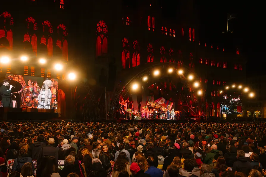 Large open-air concert in front of a red-lit historic building with a dense crowd.