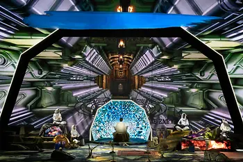 Futuristic stage installation with several performers in front of a glowing digital backdrop.