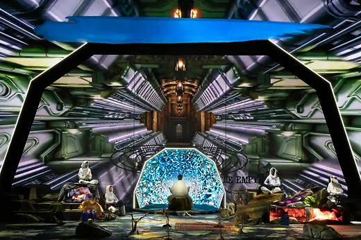 Futuristic stage installation with several performers in front of a glowing digital backdrop.