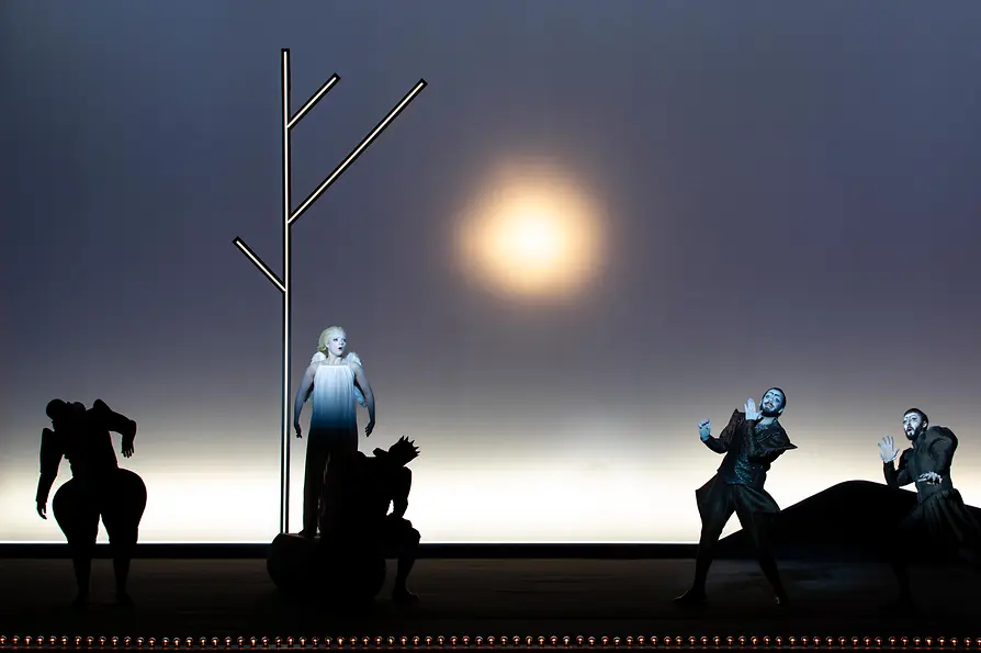 Opera scene with several performers against a minimalist stage set with a bright light source.