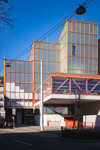 Modern Stadthallenbad building with orange glass façade and clean geometric lines.