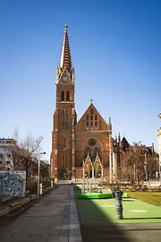 Neo-Gothic brick church with tall spire and clock against a clear blue sky.