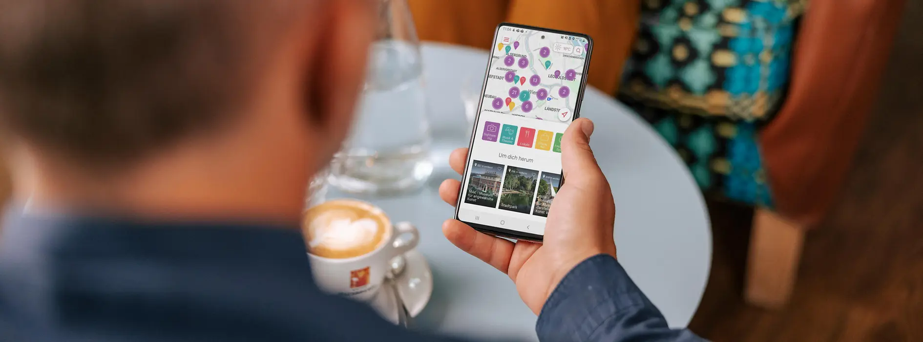 Person sitzt im Kaffee und nutzt die Smartphone-App ivie des WienTourismus mit Kartenansicht