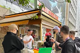 Personen stehen bei einem Wiener Würstelstand