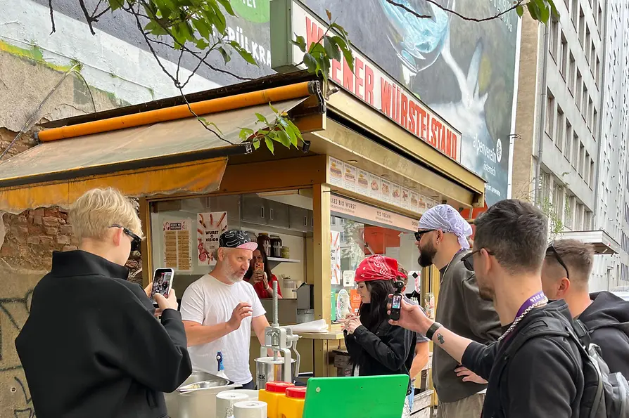 Personen stehen bei einem Wiener Würstelstand