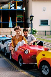 Monza children’s car ride at the Prater. A man and a woman are sitting in a red children’s car.