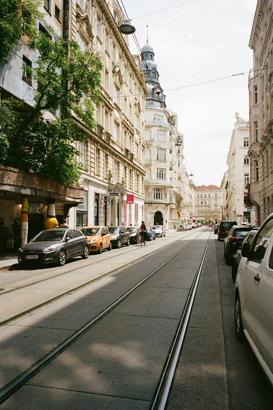 Quiet Vienna street with tram tracks, parked cars, and historic facades on a bright day.