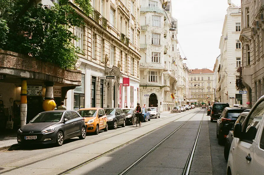 Ruhige Wiener Straße mit Straßenbahnschienen, parkenden Autos und historischen Fassaden an einem hellen Tag.