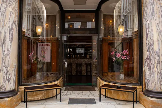 Entrance to Arici with marbled columns, large display windows, flower vases, and street reflections in the glass.