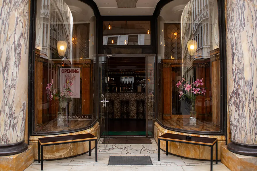 Entrance to Arici with marbled columns, large display windows, flower vases, and street reflections in the glass.