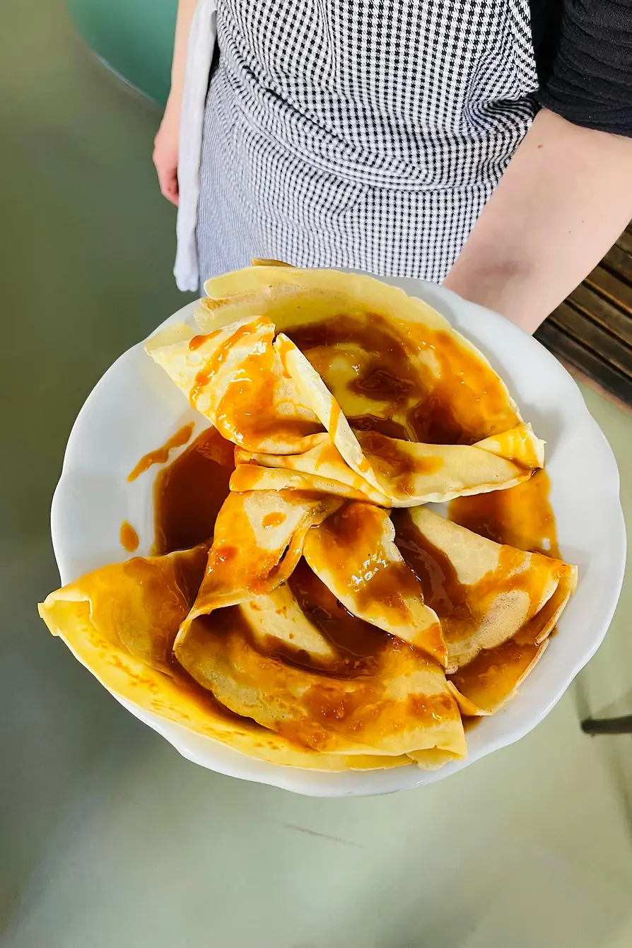 A person holds a large plate of folded crêpes generously covered in glossy caramel sauce.