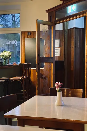 A bright dining room with wood-paneled walls, an open glass door, and small flower vases on simply set tables.