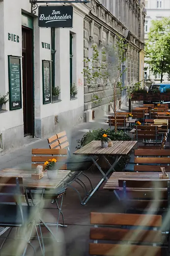 Wooden tables and folding chairs line the sidewalk outside Zum Bretschneider on a quiet street, decorated with small flowers.
