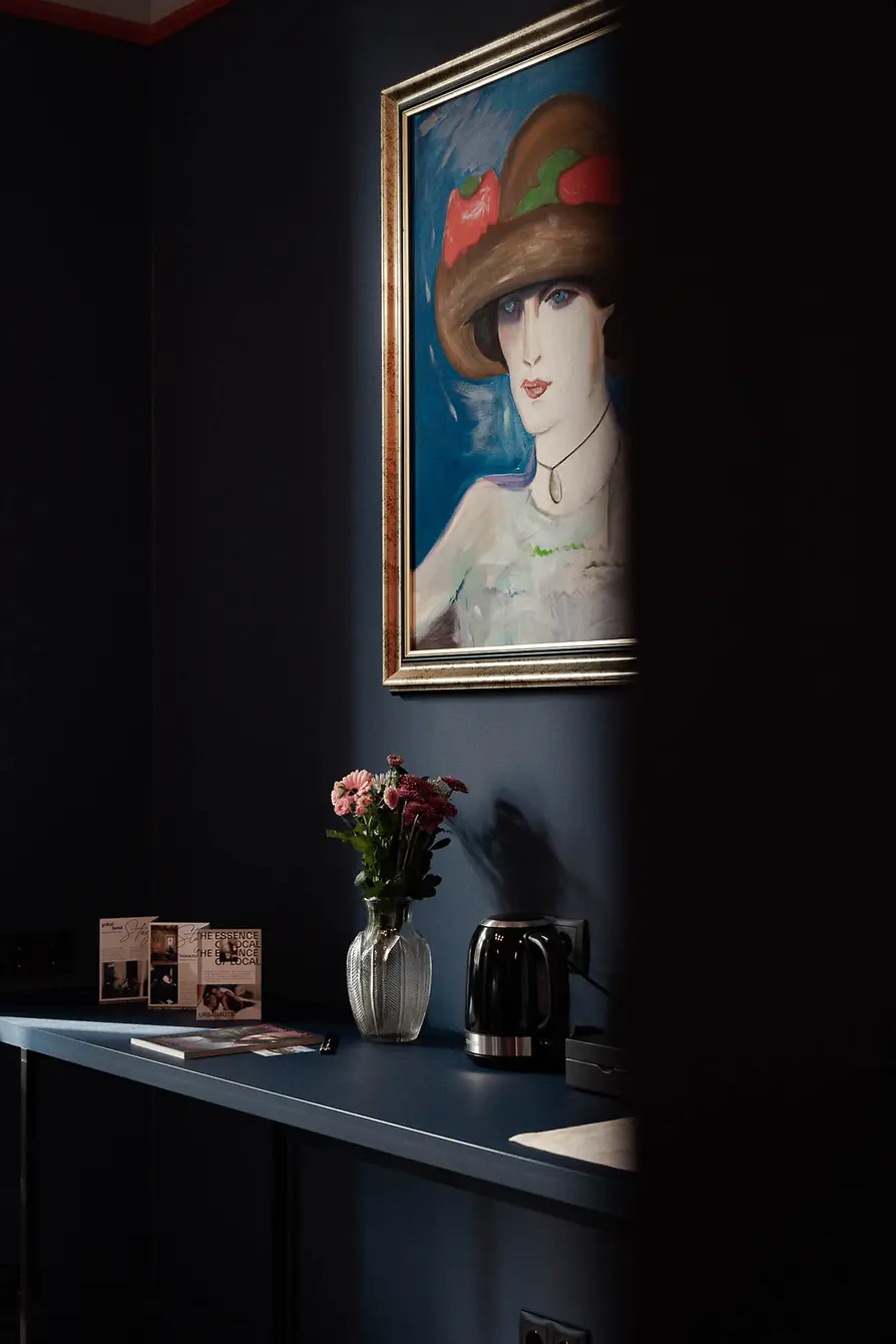 Dark room wall with a framed portrait, vase of flowers, kettle, and guest information on a console table.