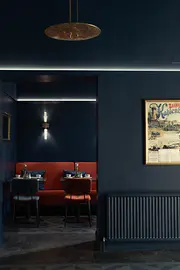 Dunkelblauer Lobbybereich mit roter Banknische, kleinen gedeckten Tischen und dezenter indirekter Beleuchtung.
