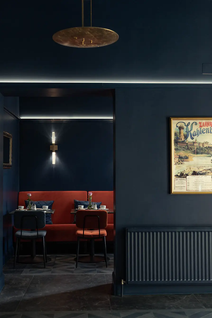 Dark blue lobby area with a red booth nook, small set tables, and subtle indirect lighting.