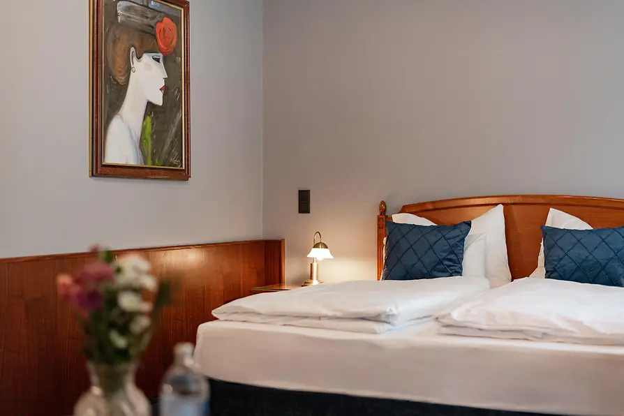 Bright bedroom with a double bed, blue cushions, wood paneling, and a portrait painting above the bed.