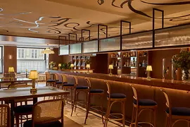 Frontalansicht einer stilvollen Hotelbar mit Hockern, beleuchteter Rückwand und auffälliger grafischer Zeichnung an der Decke.