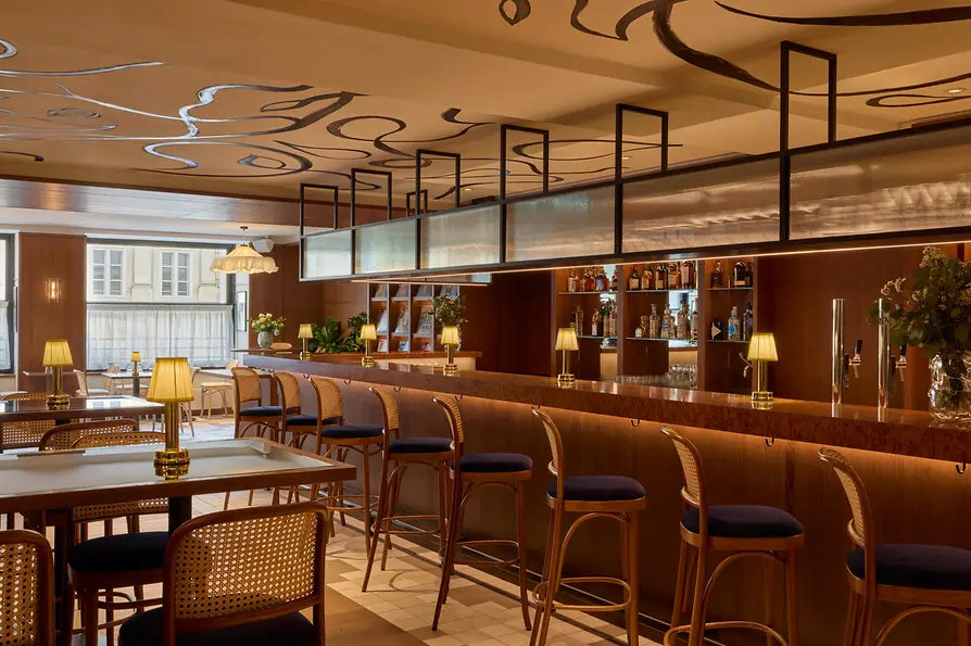 Frontalansicht einer stilvollen Hotelbar mit Hockern, beleuchteter Rückwand und auffälliger grafischer Zeichnung an der Decke.