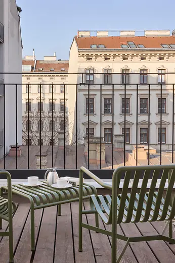 Private terrace with green chairs, a small table, and coffee service overlooking historic Viennese building facades.