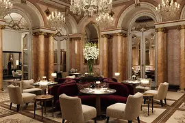 Opulenter Speisesaal mit Marmorsäulen, Kristalllüstern, Spiegeln und elegant gedeckten Tischen in historischem Ambiente.