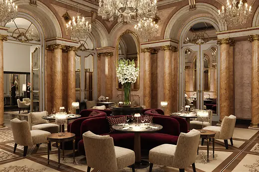 Opulent dining room with marble columns, crystal chandeliers, mirrors, and elegantly set tables in a historic setting.