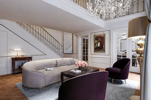 Elegant living area of a duplex suite with a curved sofa, chandelier, staircase, and classic wall detailing.