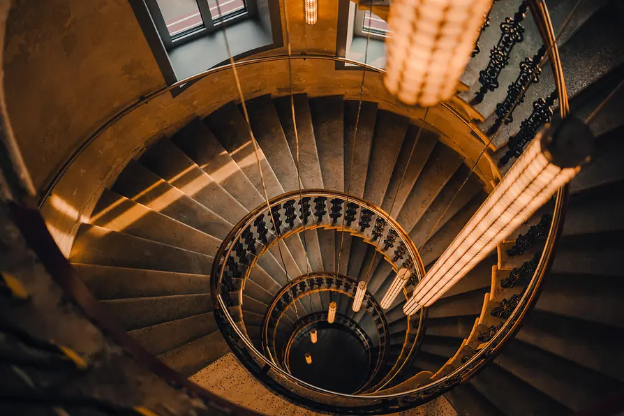 Top-down view into a curved staircase with dark railings and warmly glowing pendant lights at the center.