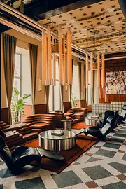 Stilvoller Lounge-Bereich mit braunen Ledersofas, schwarzen Sesseln, langen Hängeleuchten und gemustertem Boden.