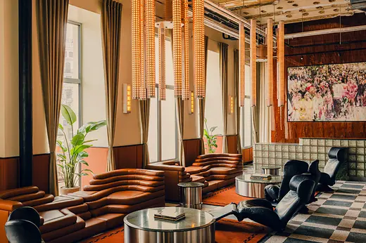 Stylish lounge area with brown leather sofas, black armchairs, long pendant lights, and a patterned floor.