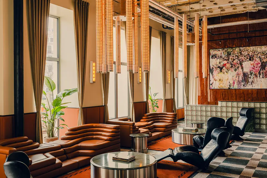 Stilvoller Lounge-Bereich mit braunen Ledersofas, schwarzen Sesseln, langen Hängeleuchten und gemustertem Boden.