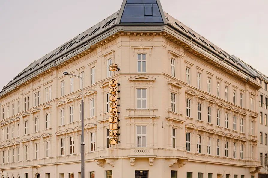 Helles Eckgebäude mit historischer Fassade, modernem Dachaufbau und vertikalem „The Companion“-Schriftzug an einer ruhigen Straßenkreuzung.